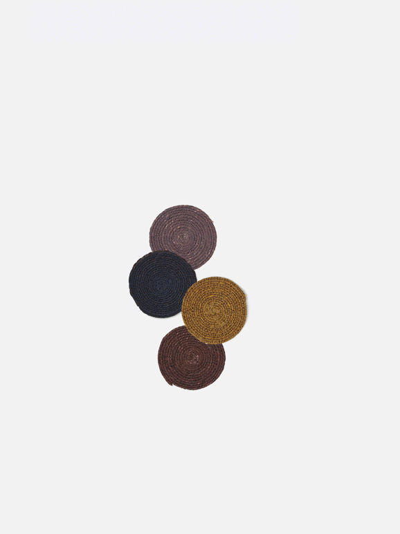 Four round woven coasters in different colors on a light beige background