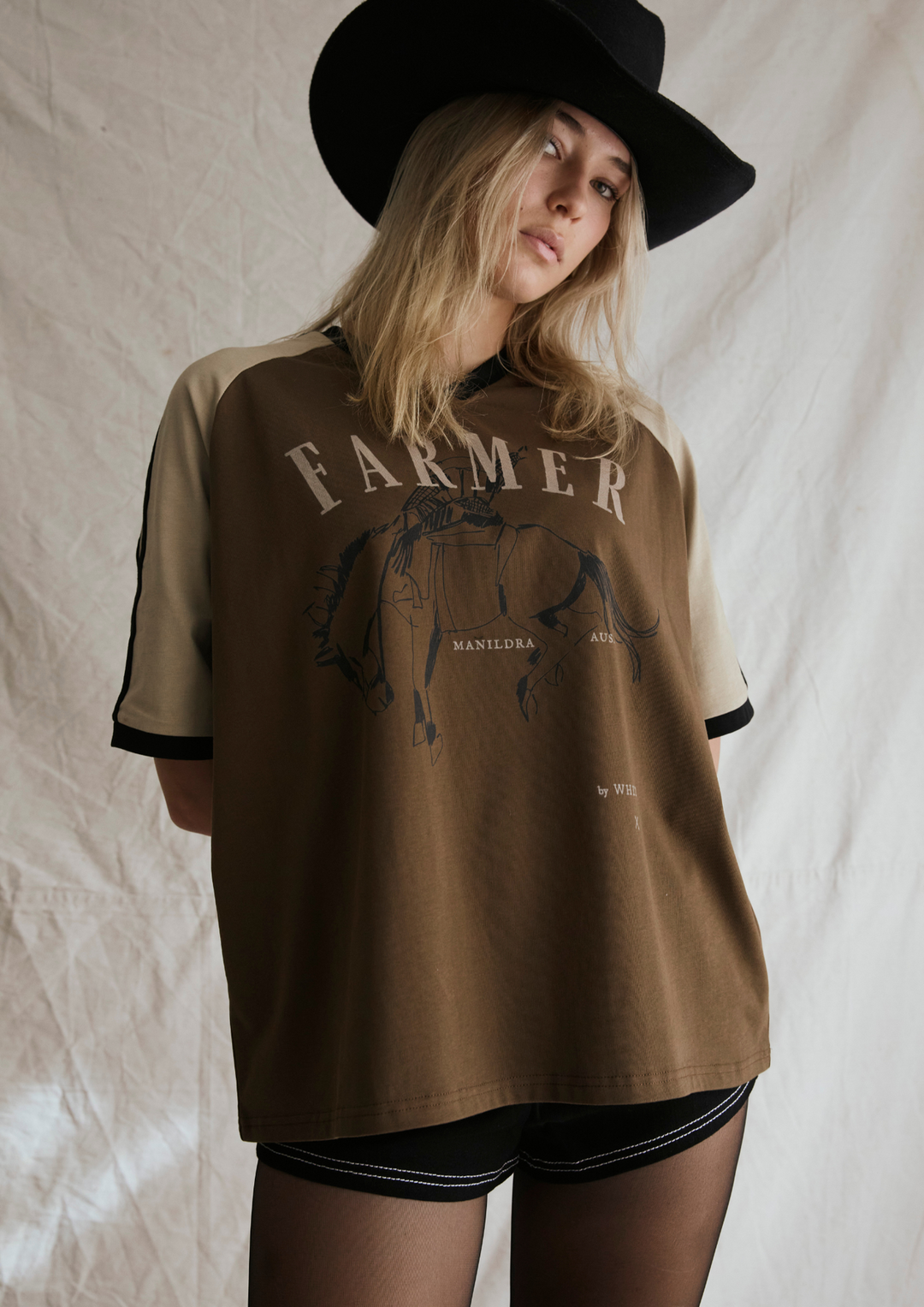 Person wearing a brown 'Farmer' t-shirt with a graphic design on a plain background