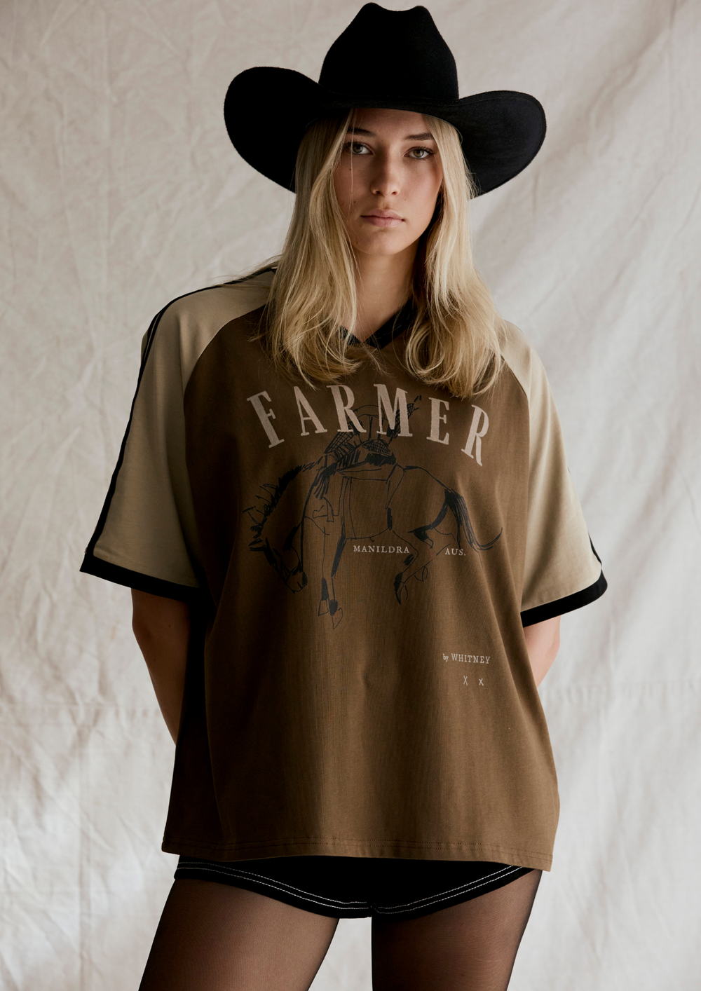 Person wearing a brown 'Farmer' t-shirt with a graphic design on a neutral background