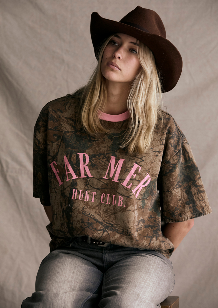 Person wearing a camouflage t-shirt with 'FAR MER HUNT CLUB' text and a brown cowboy hat.
