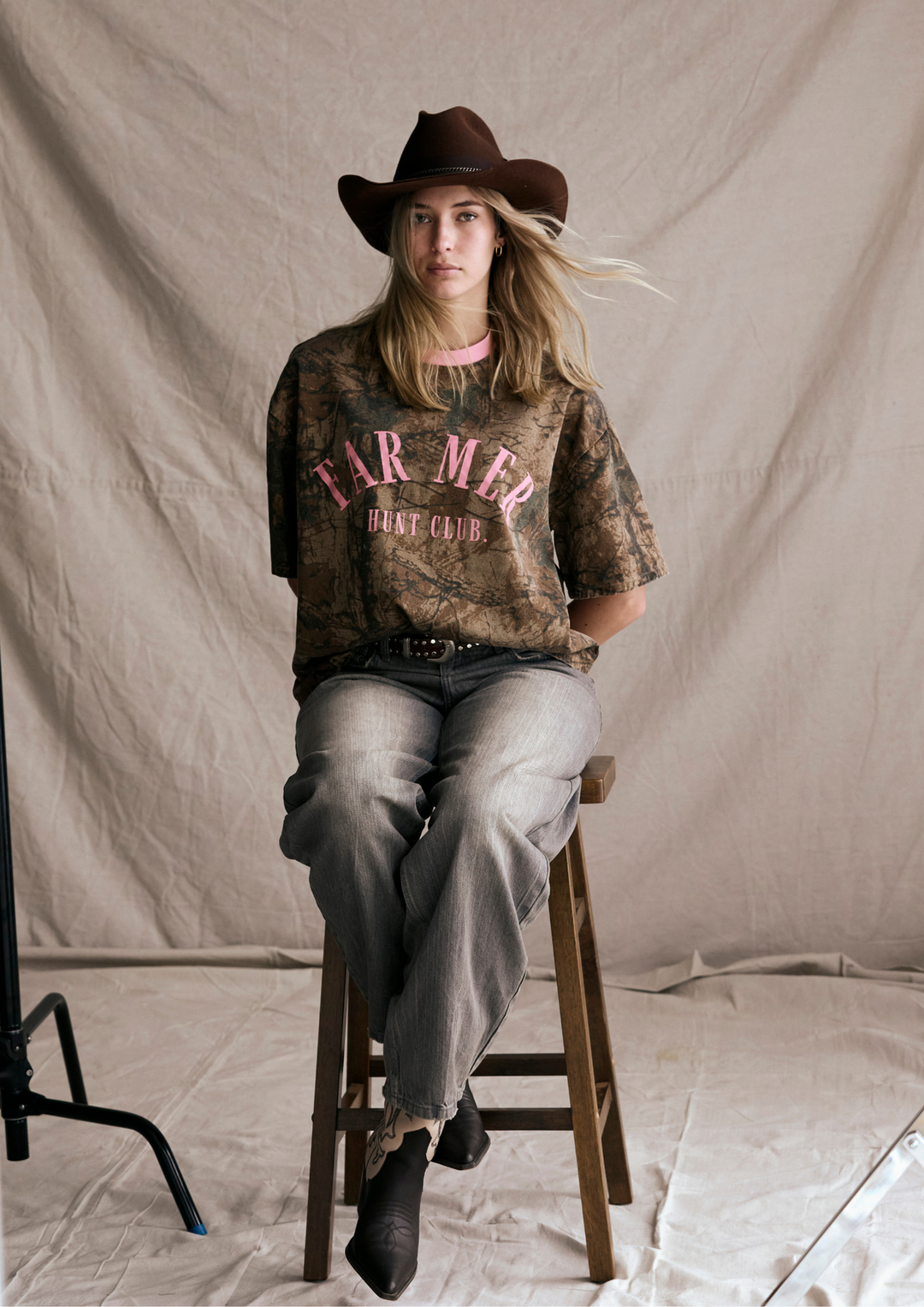 Person wearing a cowboy hat and 'Farmer Diet Club' t-shirt sitting on a stool against a plain background